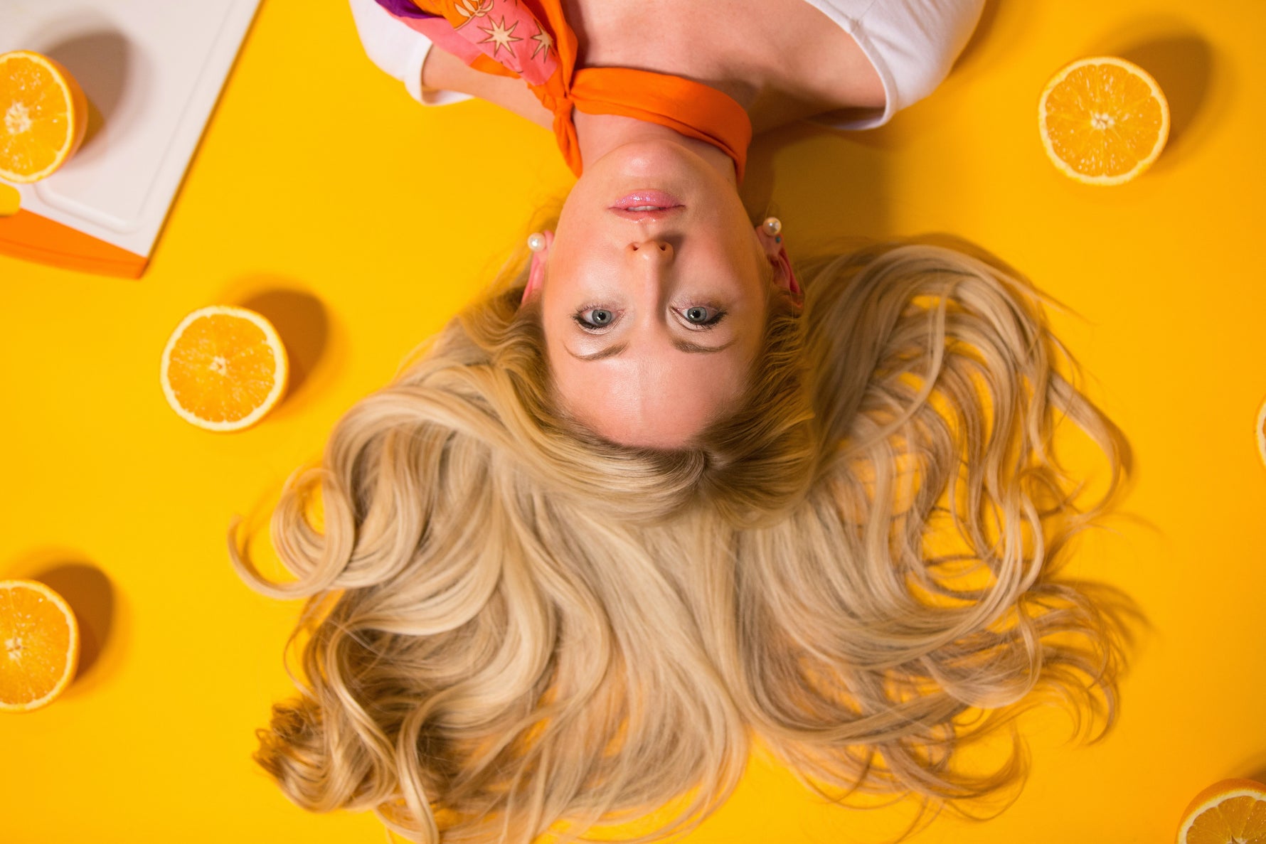Blonde woman lying on a yellow background surrounded by orange slices
