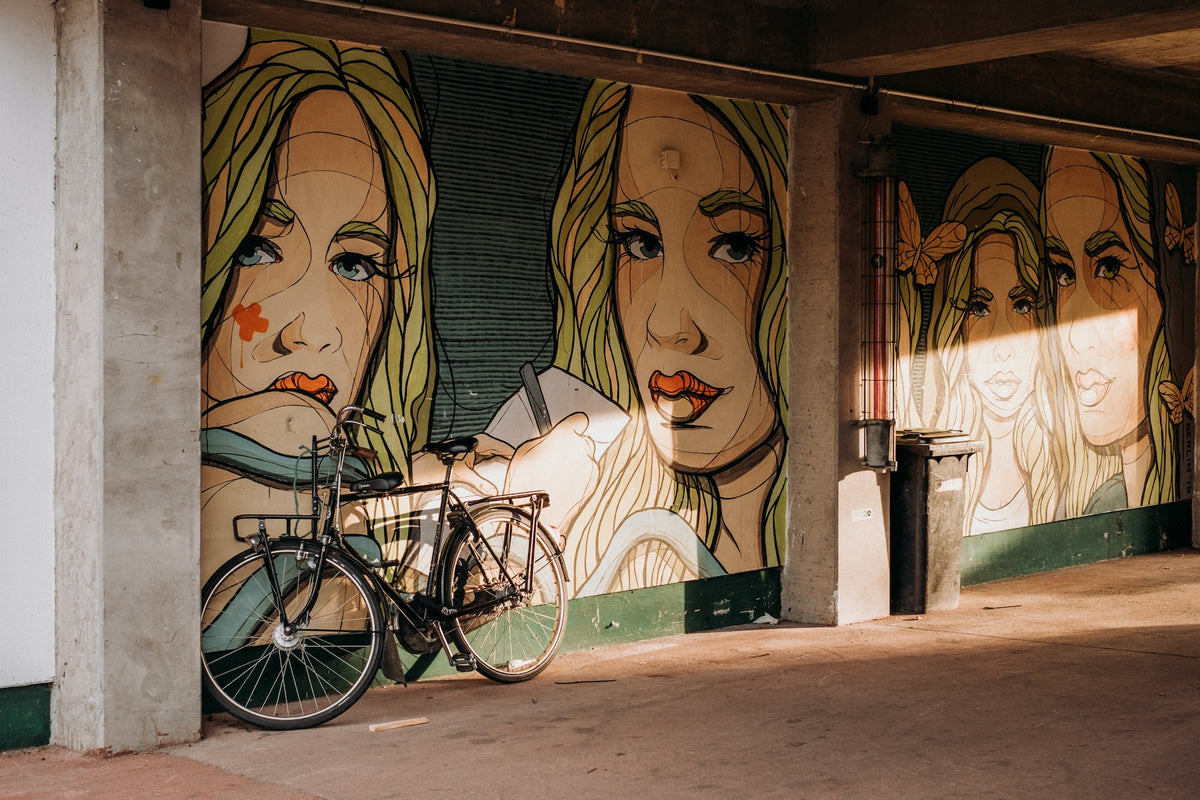Street mural of three women's faces with a bicycle parked in front