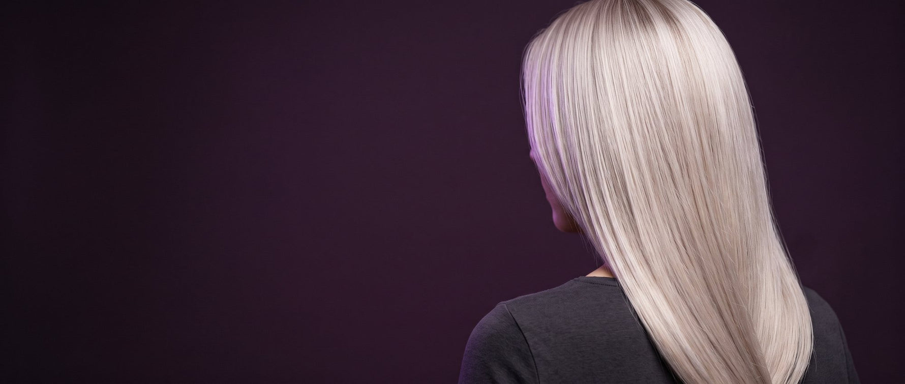 Back view of a woman with long platinum blonde hair against a dark purple background