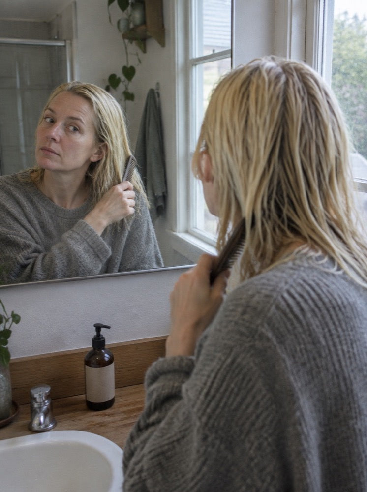Combing through damp hair at the mirror