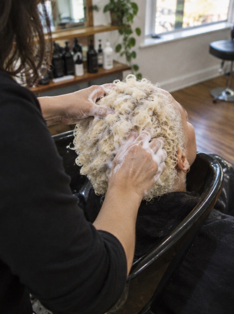 Working lather through bleached curls at the basin